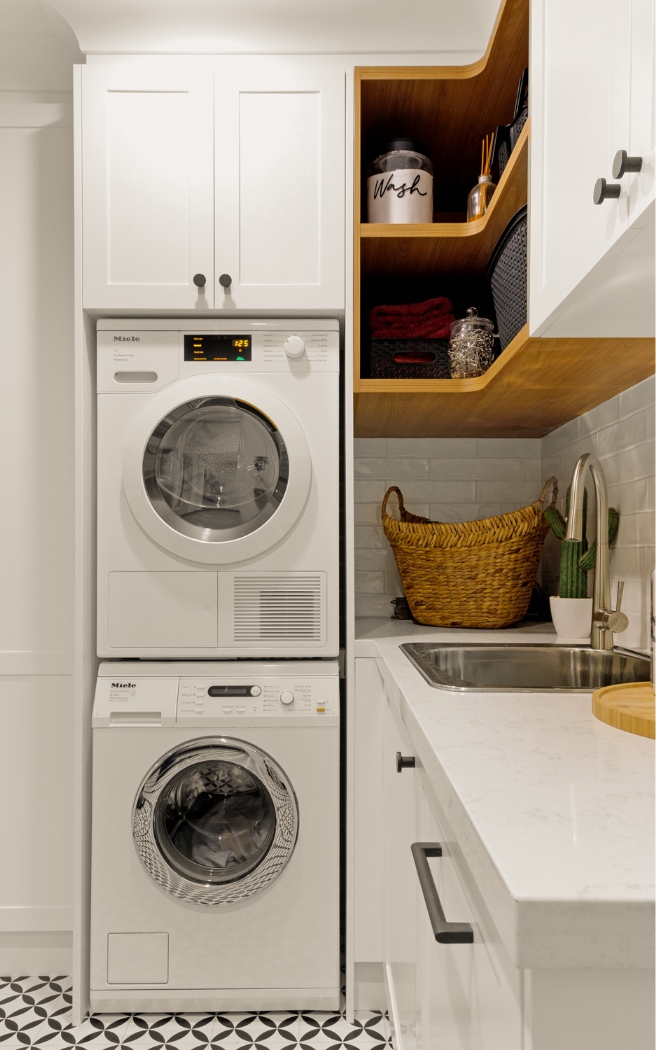 Built-in laundry with stacked washer and dryer, timber shelving and stone benchtop